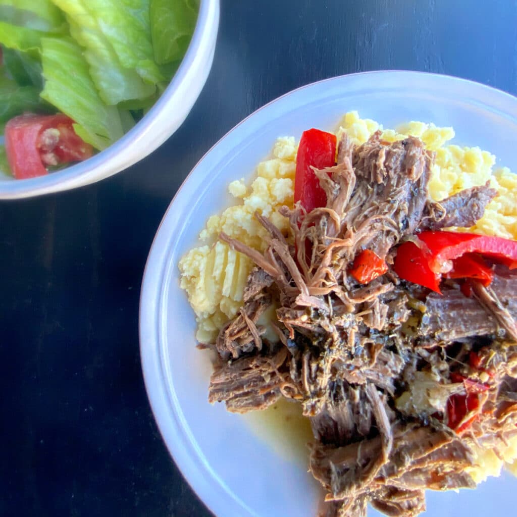 Roast beef with pepper plates on top of mashed potatoes with a side salad off the to the left