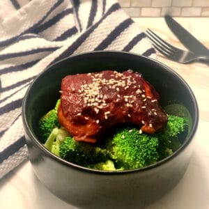 finished thigh on a bed of broccoli in a black round bowl with sesame seeds sprinkled on top