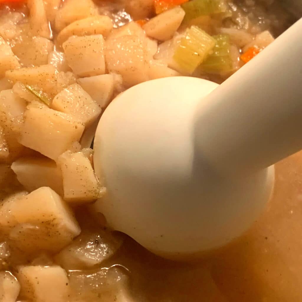 image of cooked potatoes in crockpot with immersion blender about to start