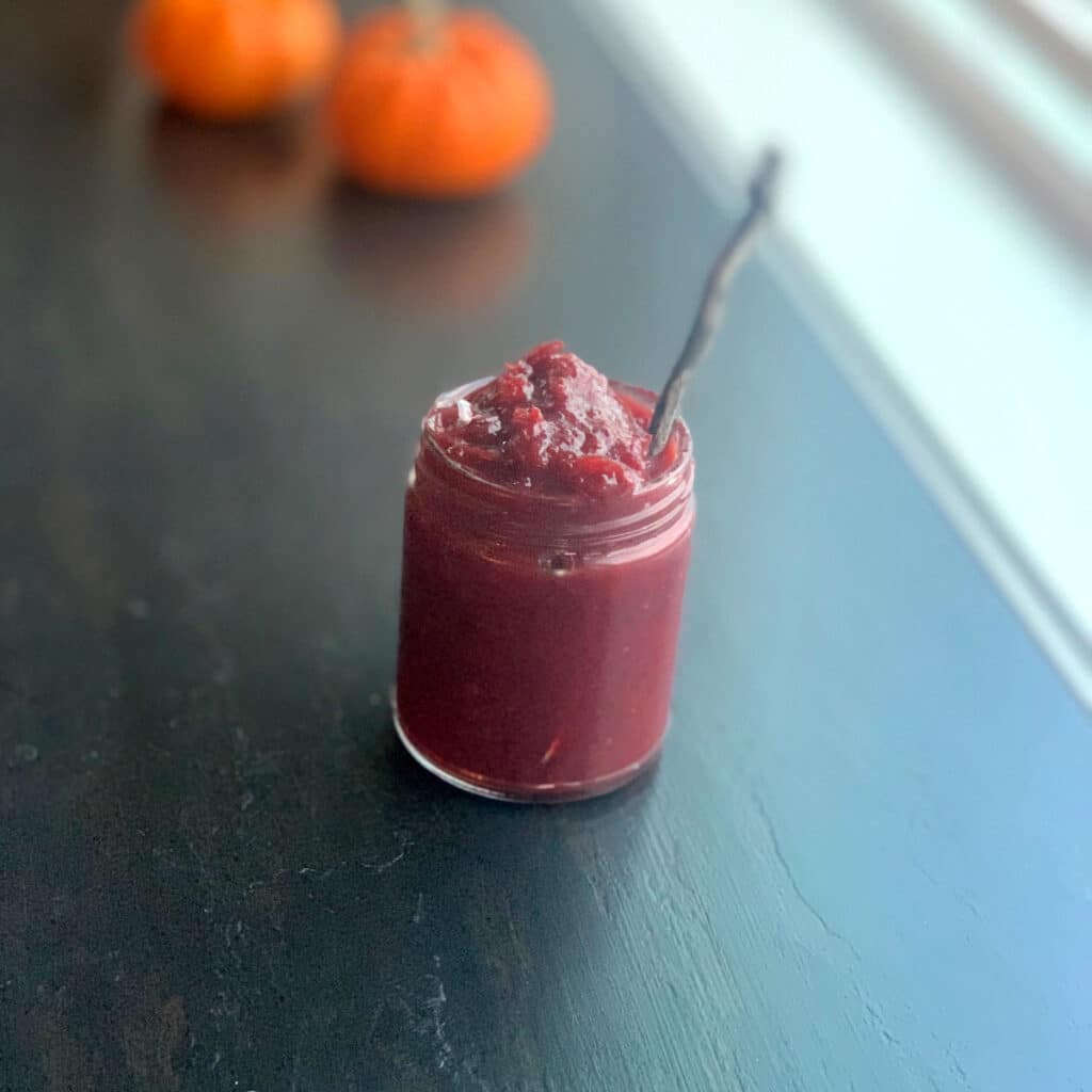 sauce in a glass jar with a spoon and some pumpkins blurred in the background