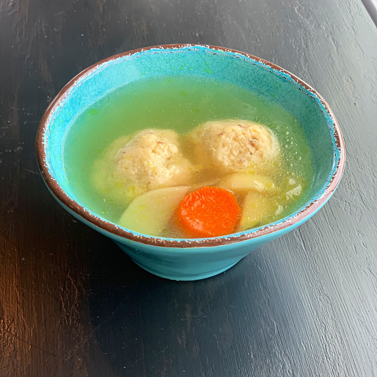 chicken soup in a round turquoise bowl with two matzo balls, carrots and parsnips