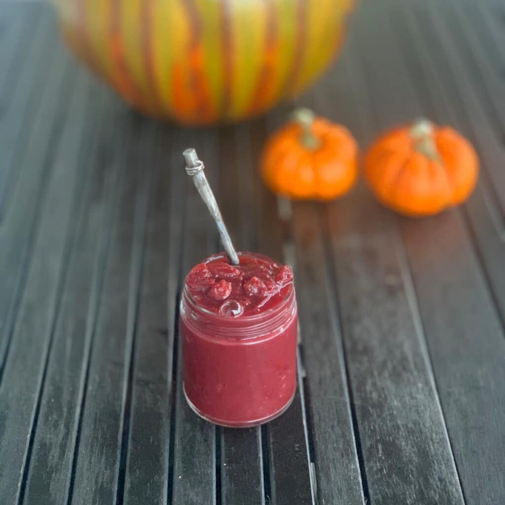 glass jar on a black slatted surface with pumpkins in background
