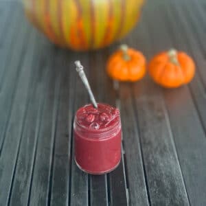 glass jar of sauce on a black slatted surface with pumpkins in background