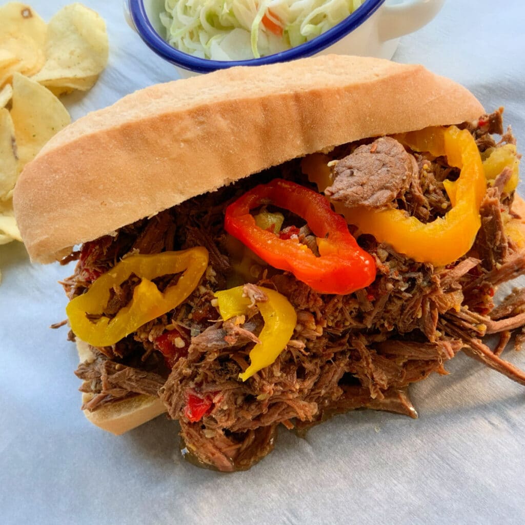 hoagie roll with beef and pepper with chips and cole slaw in the background