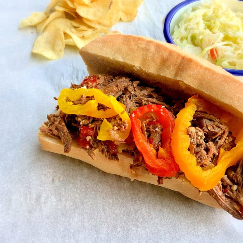 Slow cooker beef sandwich on a hoagie roll with cole slaw and chips