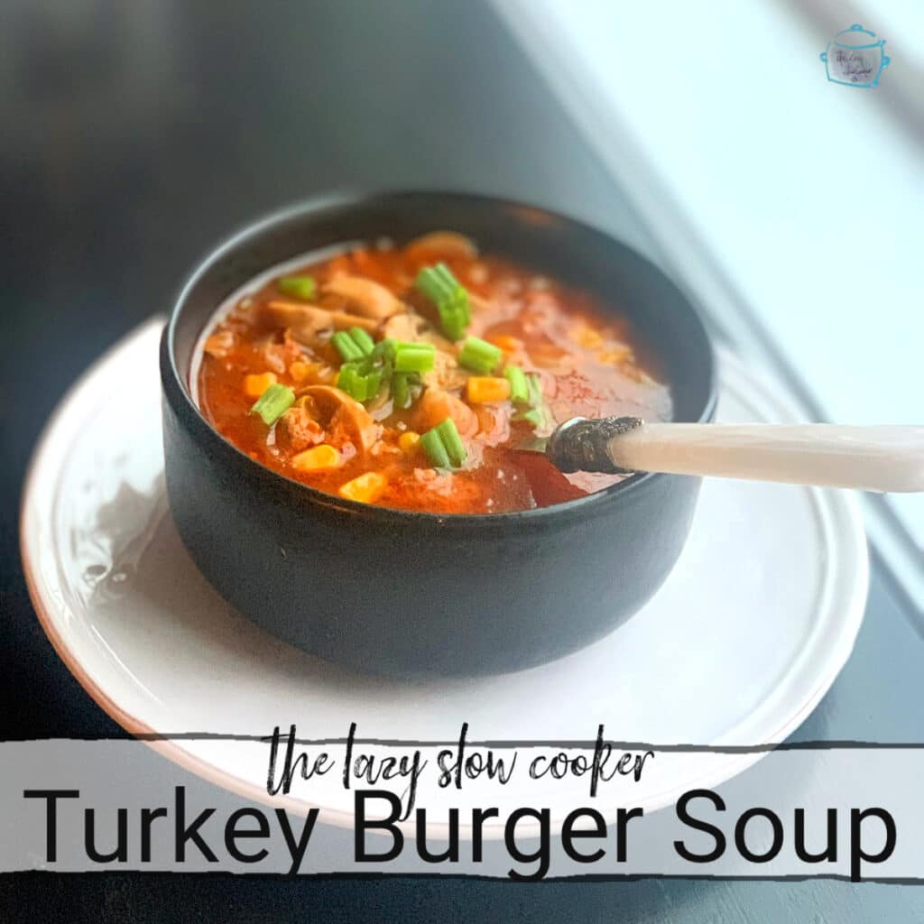 a tomato colored soup with mushrooms and corn kernels visible. Green onion is sprinkled on top. In a round black bowl on a window sill