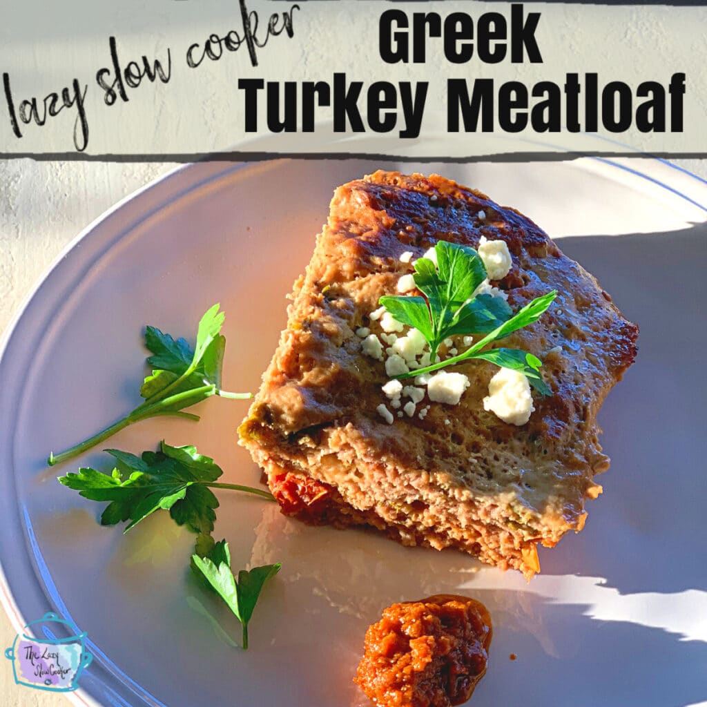 top view of a piece of turkey meatloaf with some crumbled feta and fresh parsley on top. a dollop of sun dried tomato pesto is on the round white plate next to it.