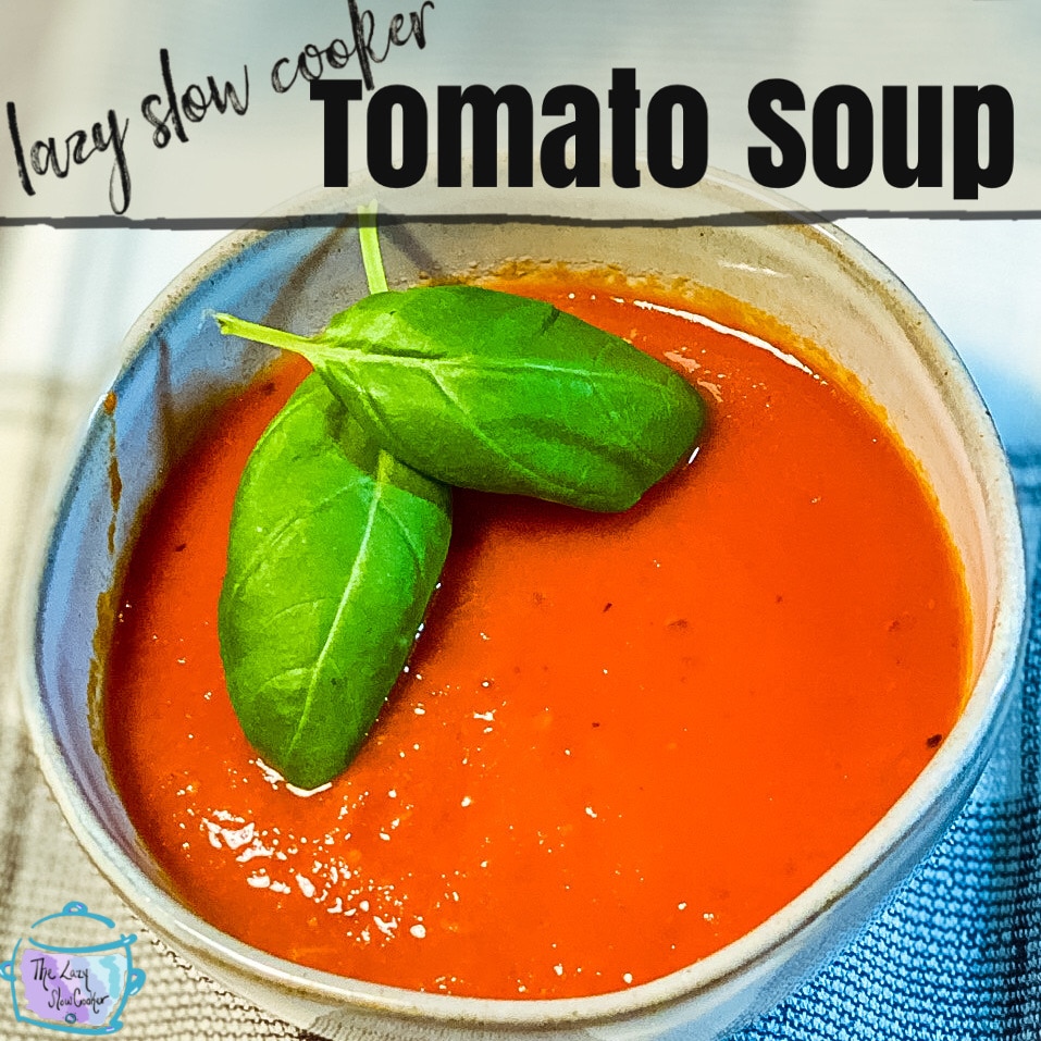 round gray bowl filled with tomato red soup and two green basil leaves as garnish