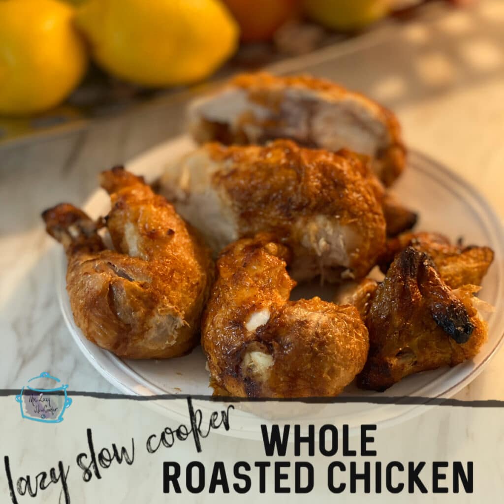 chicken legs and breasts with skin on a white round plate with some fruit blurred in the background