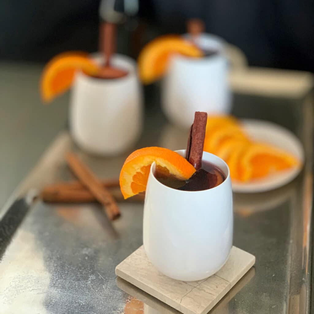 three while glasses filled with mulled wine with orange wedge and cinnamon sticks as garnish