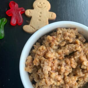 Gingerbread oatmeal with cinnamon sprinkled one top with a cooked and some red and green gingerbread shaped gummies off the side