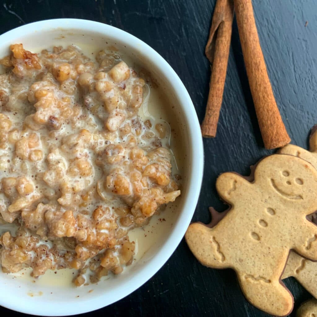 Oatmeal in a round white bowl with cream poured on top and some gingerbread cookies stacked on the side.