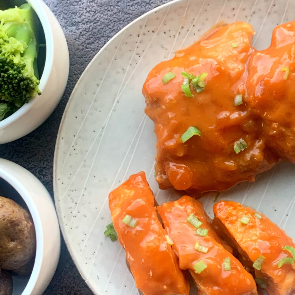 close up view of sliced chicken breast and a whole thigh covered in apricot sauce with green scallion for garnish