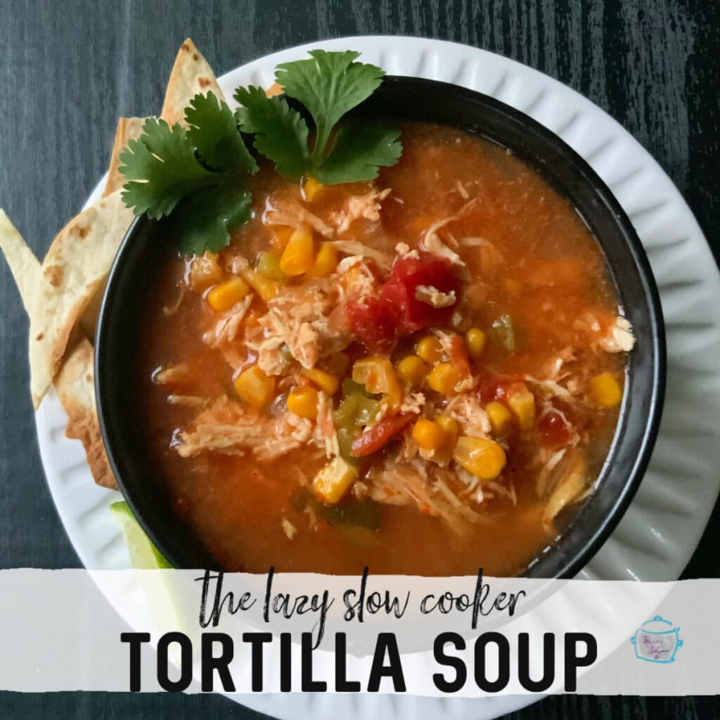 Black bowl of slow cooker chicken tortilla soup with some pits off to the side