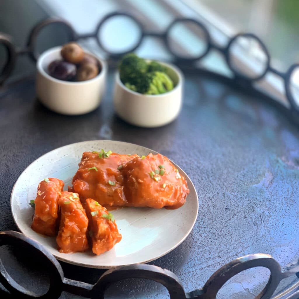 distance view of apricot chicken on a round white plate with broccoli and potatoes in the background