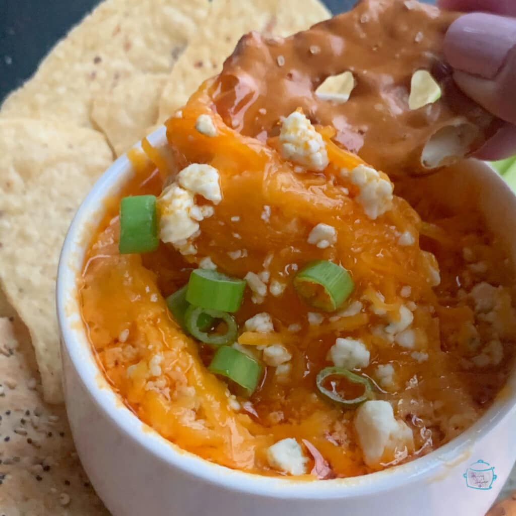 A small round dish of dip with a pretzel being dipped into it.