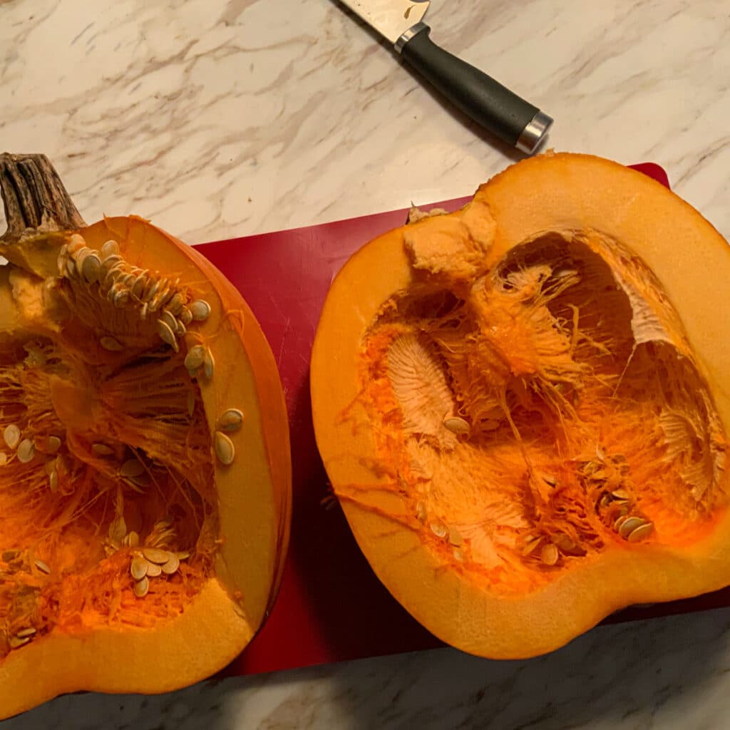 Pumpkin cut in half laying on a red cutting mat with the seeds still inside.  