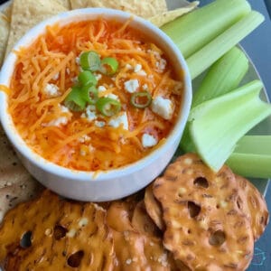 A white bowl filled with dip off to the left with celery and pretzels around it