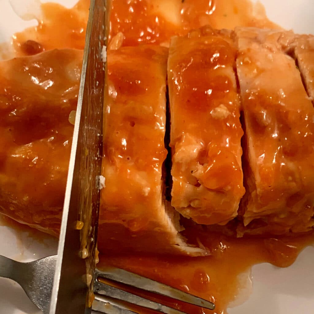 close up of cooked chicken breast with sauce beling sliced by a large knife