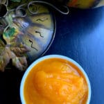 A round white bowl of pumpkin purée on a black table with a metal pumpkin off to the side