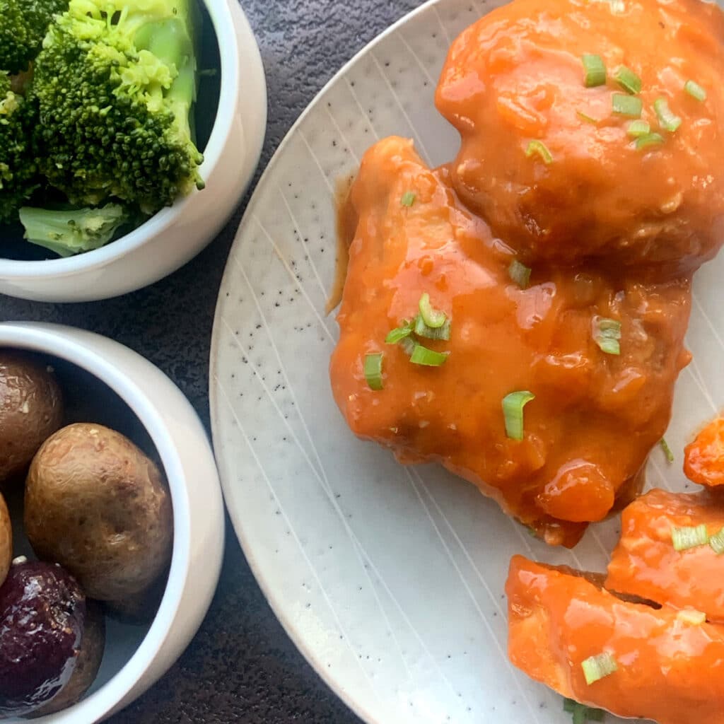 Close up of chicken thighs with creamy apricot sauce. Broccoi and potatoes are on different plates in the background