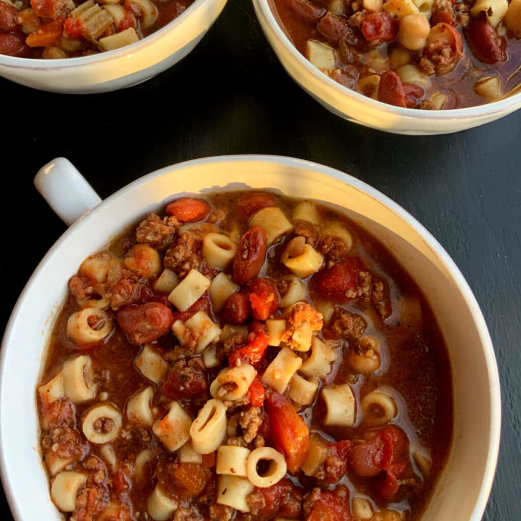 Three bowl of pasta e fagioli in round white bowls on a black surface from the top down