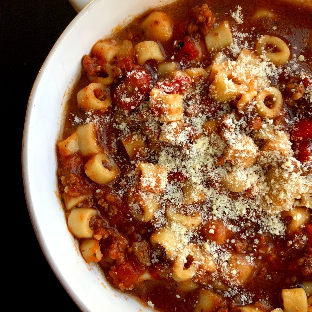 Close up of a bowl of pasta e fagioli with grated parmesan cheese on top in a white, round bowl