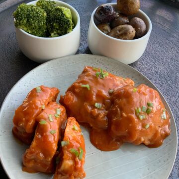 Apricot chicken on a round gray plate with a bowl of mini potatoes and a bowl of broccoli in the background