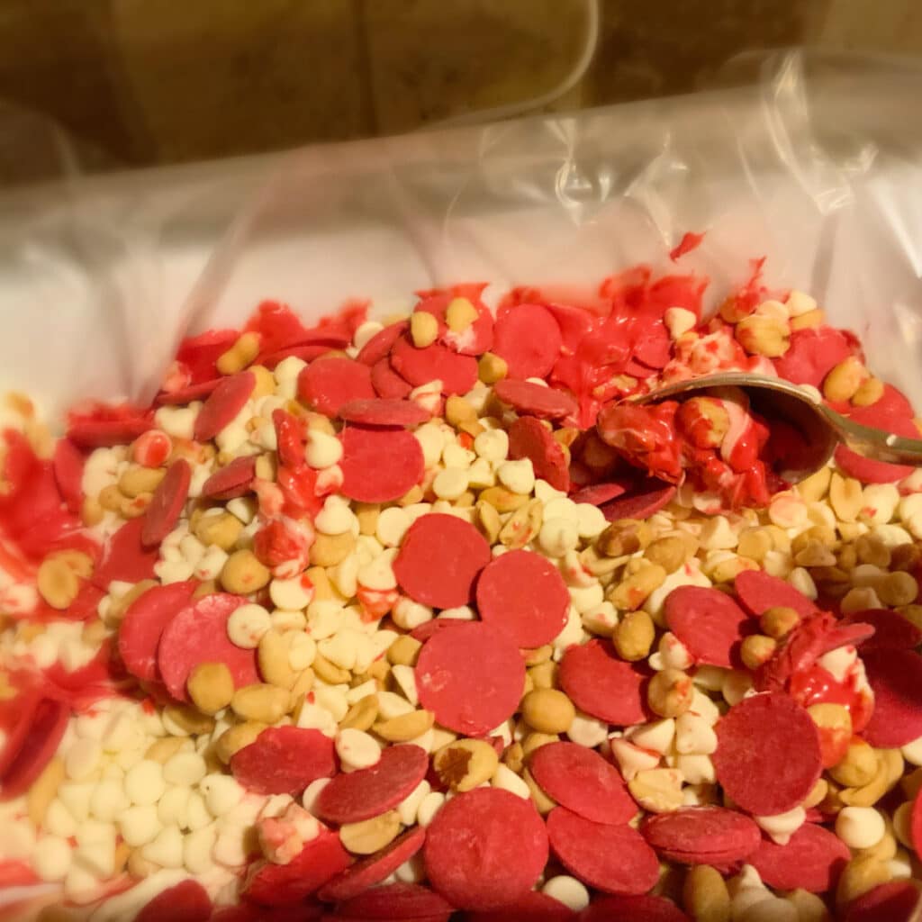 nuts and candy pieces in slow cooker starting to melt and being stirred by a wooden spoon