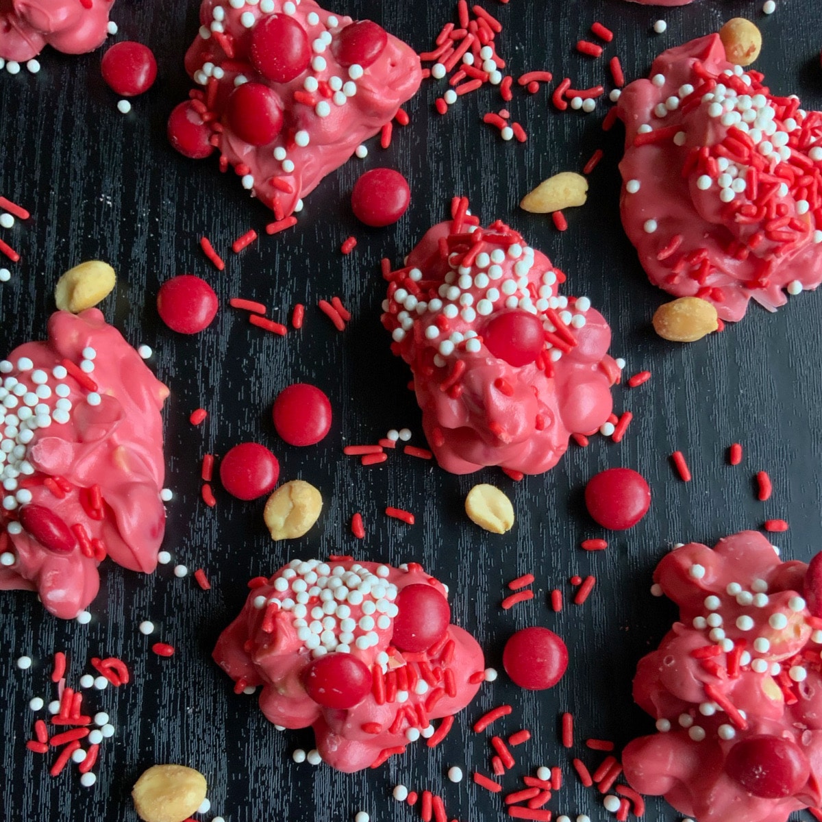 red crockpot candy on a black surface surrounded by sprinkles and nuts