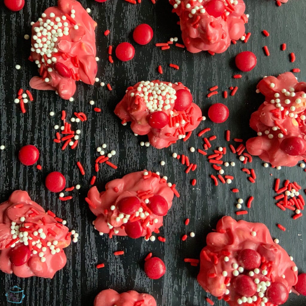 pink chocolate candy with red candy decoration and sprinkles laying all around 