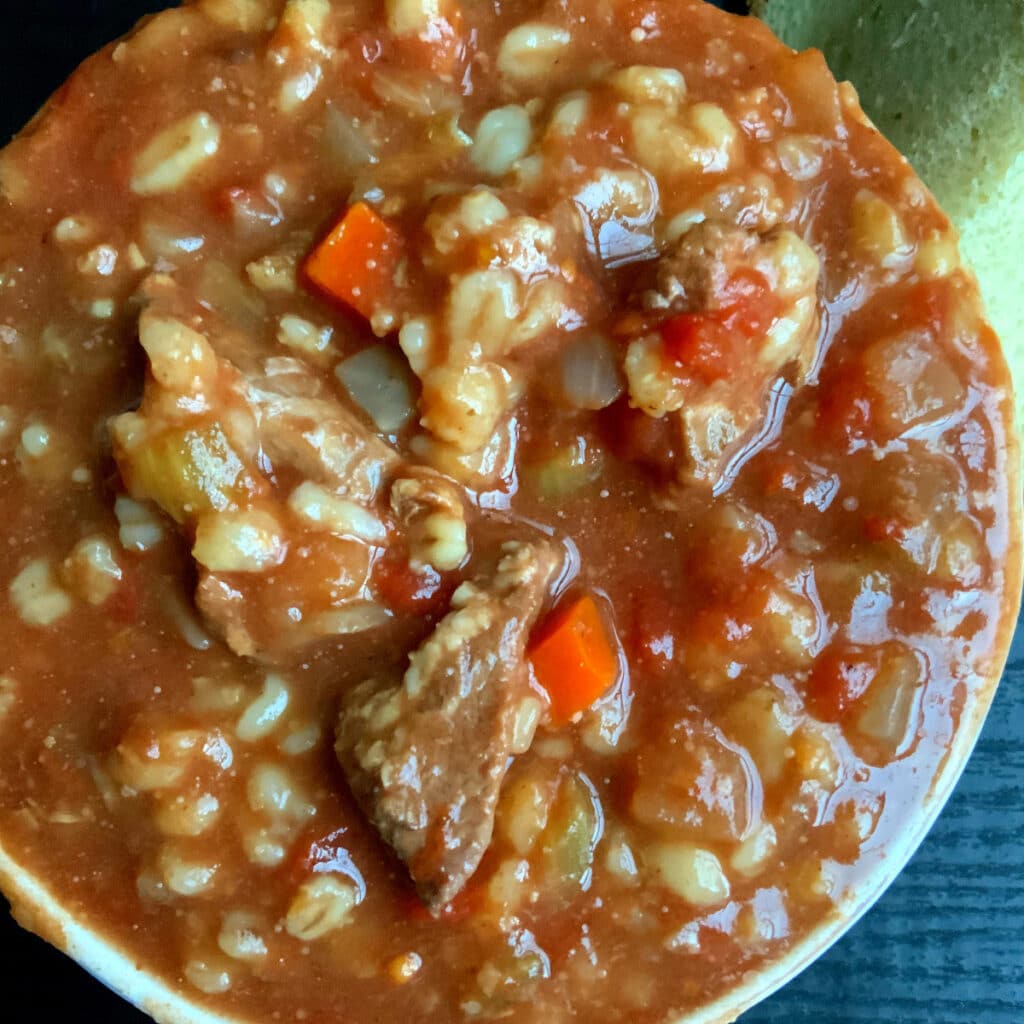 Looking down on a bowl of soup with beef, barley and veggies visable