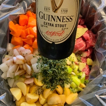 Ingredients for stew in slow cooker with a bottle of Guinness held in front of it