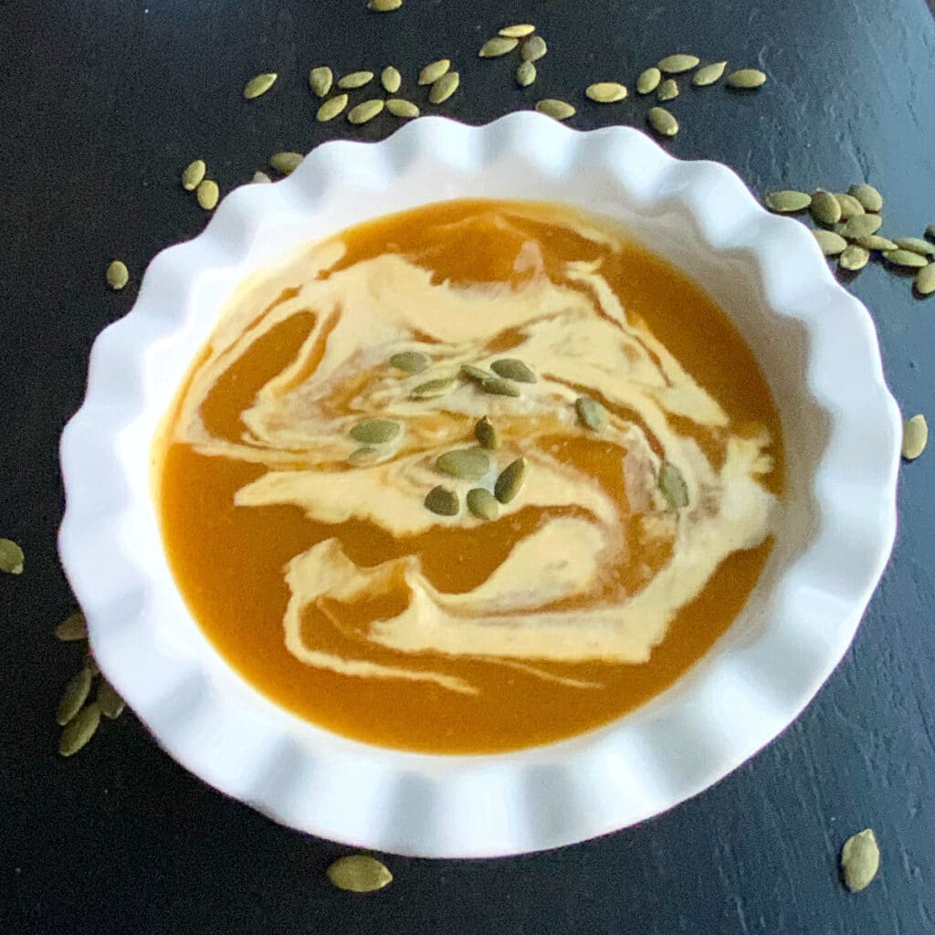 side view of a round white bowl filled with thick looking soup with some cream swirled in