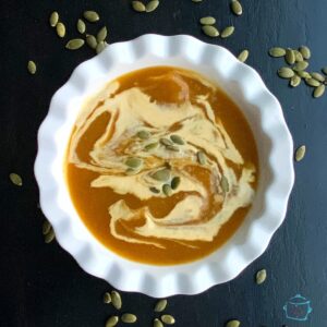 round white bowl of pumpkins soup drizzled with cream and some pumpkin seeds