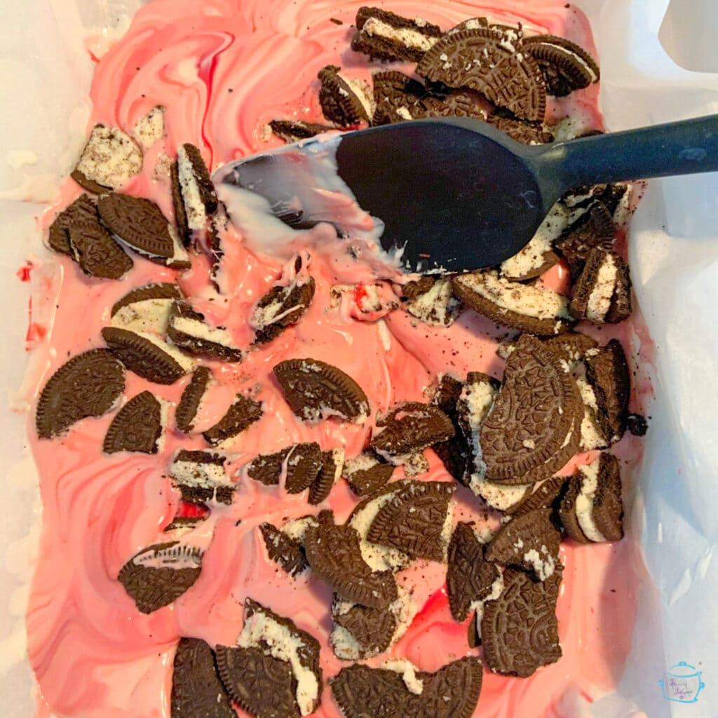 Melted pink chocolate being stirred together with crushed oreos using a large black spoon