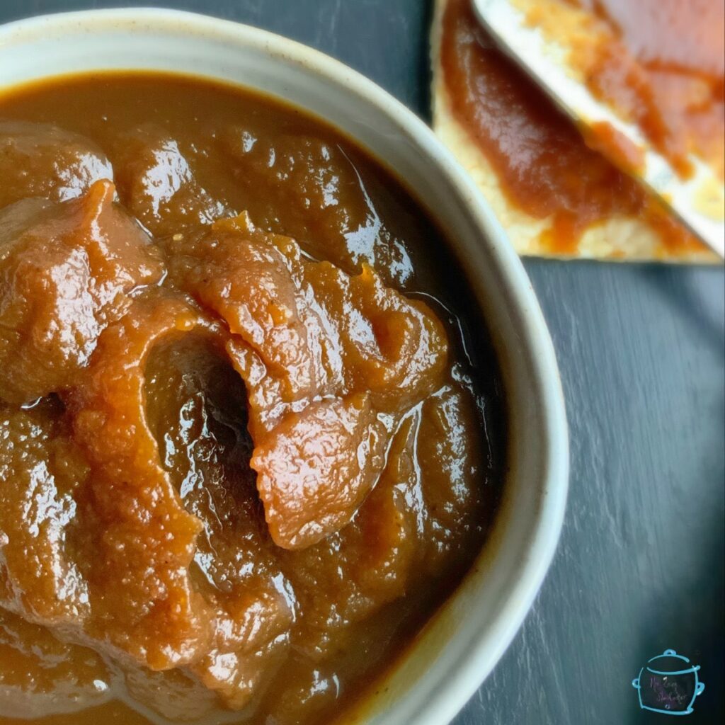 A bowl of pumpkin butter a knife and cracker in background