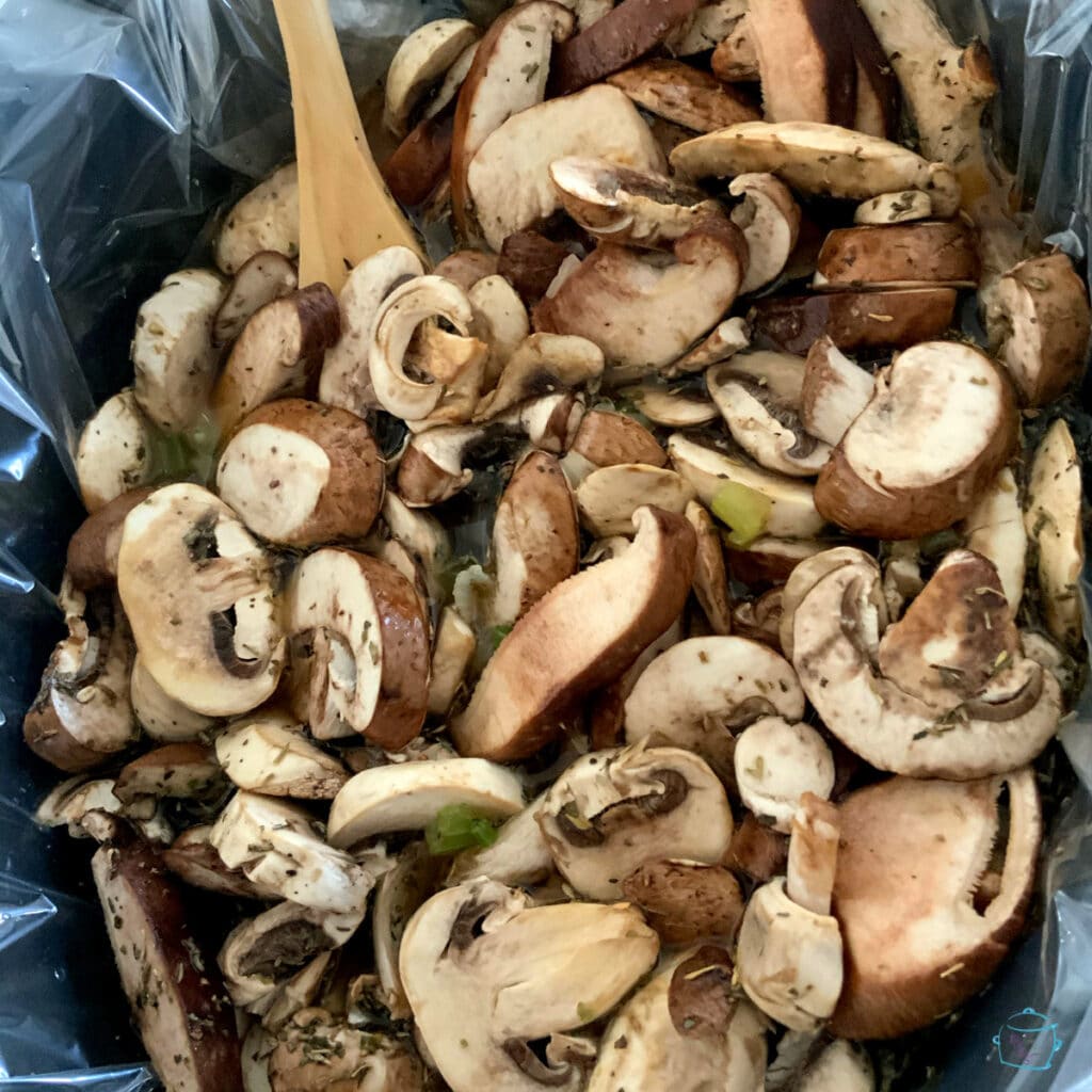 Sliced mushrooms in a crockpot with a wooden spoon