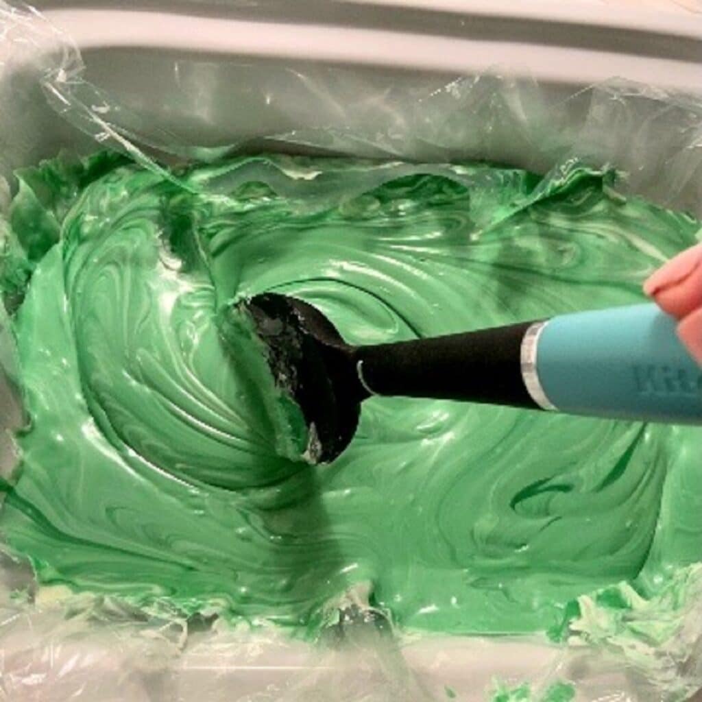 melted green chocolate being stirred by a big black spoon with a turquoise handle