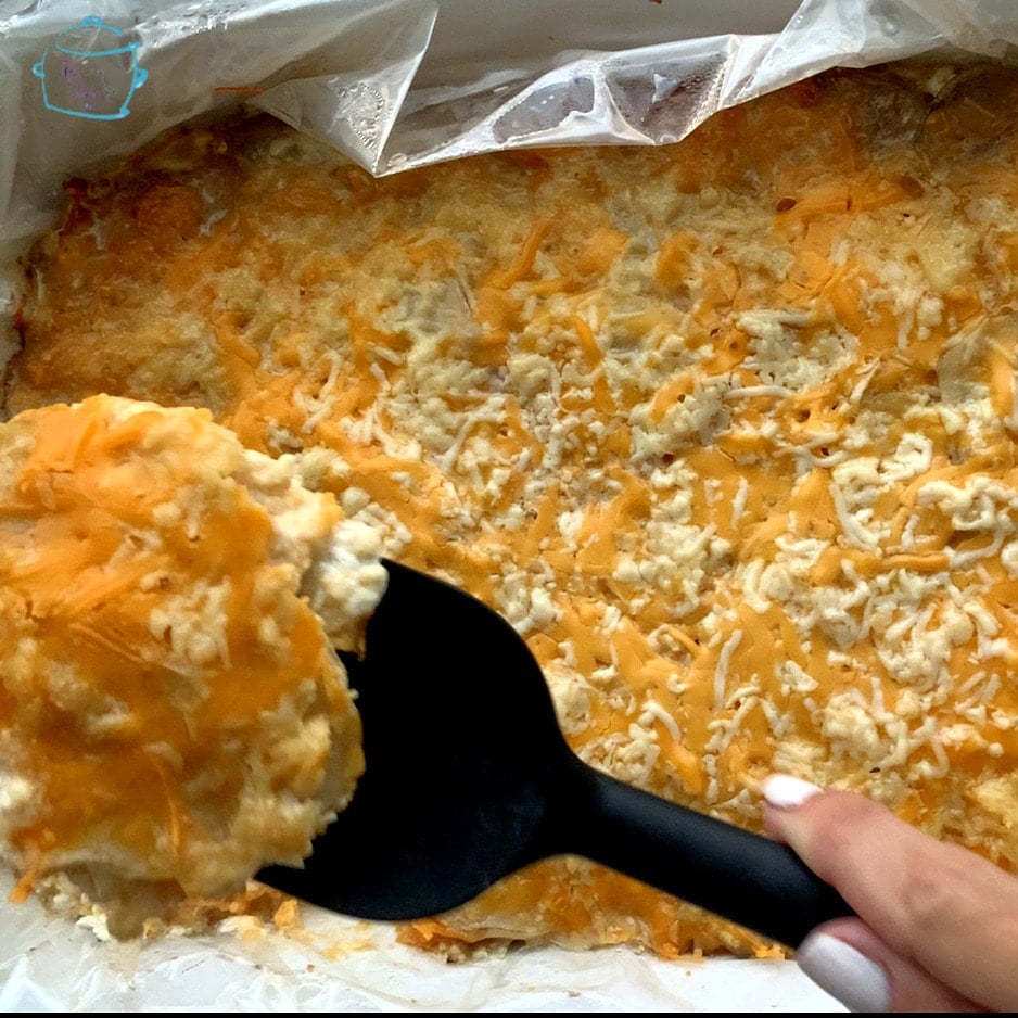 A crockpot full of cooked potatoes with a top layer of melted cheese. Some of the dish i being lifted up by a spatula