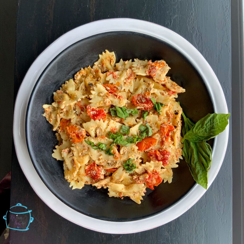 Close up of bow tie pasta coated in cheese with tomatoes and fresh basil on a plate