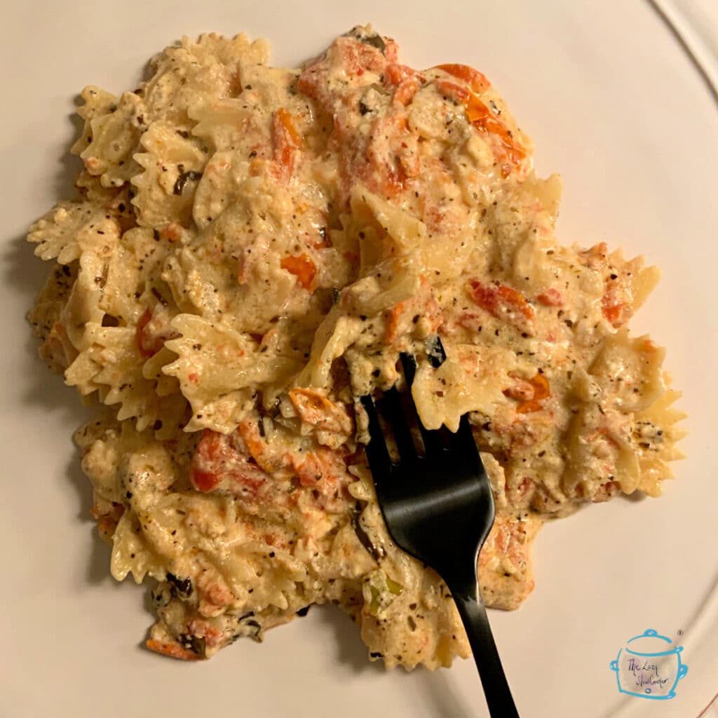 Close up of bow tie pasta coated in cheese with tomatoes and fresh basil on a plate