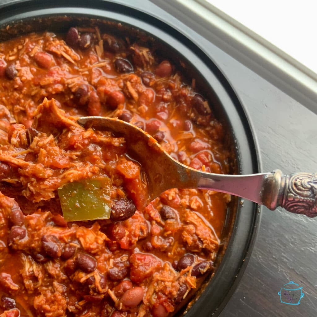 A around black bowl filled with chili with a spoon picking some of it up.