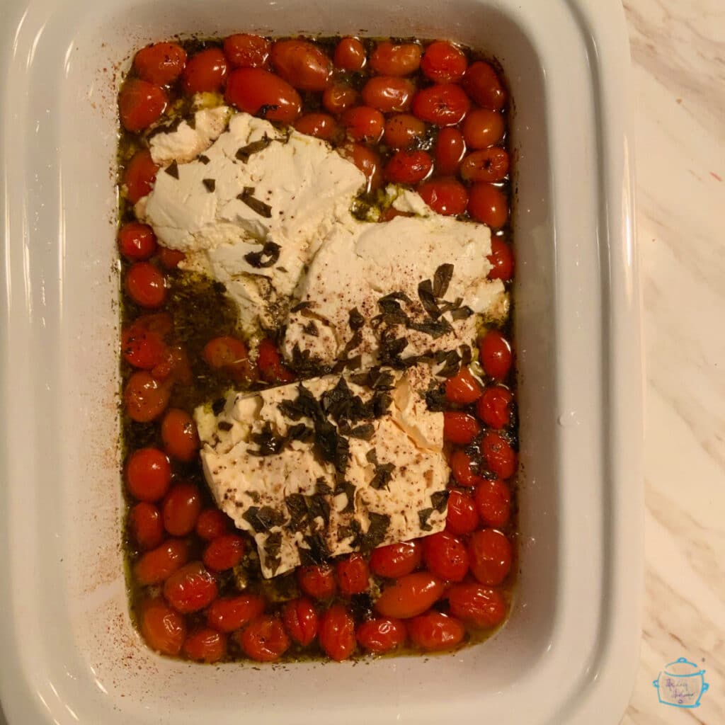 Grape tomatoes, chunks of white cheese and seasonings in a white, rectangular crockpot