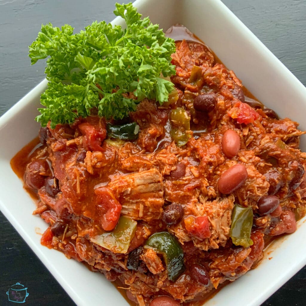 A square bowl filled with shredded chucks of beef and veggies in a thick red sauce garnished with parsley