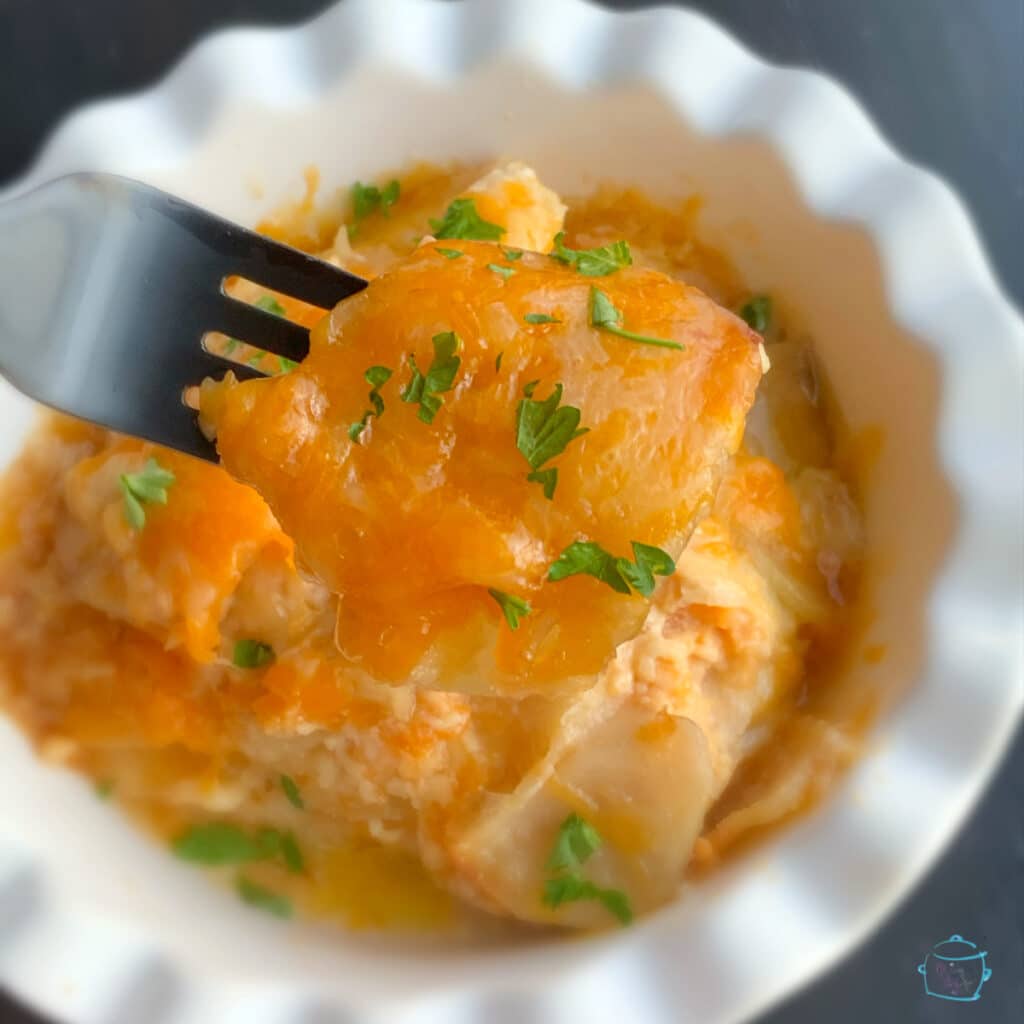 Slow cooker cheesy scalloped potatoes on a fork with more potatoes blurred in the background