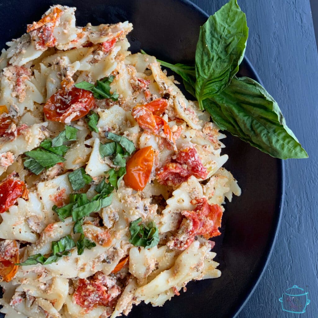Close up of bow tie pasta coated in cheese with tomatoes and fresh basil on a plate