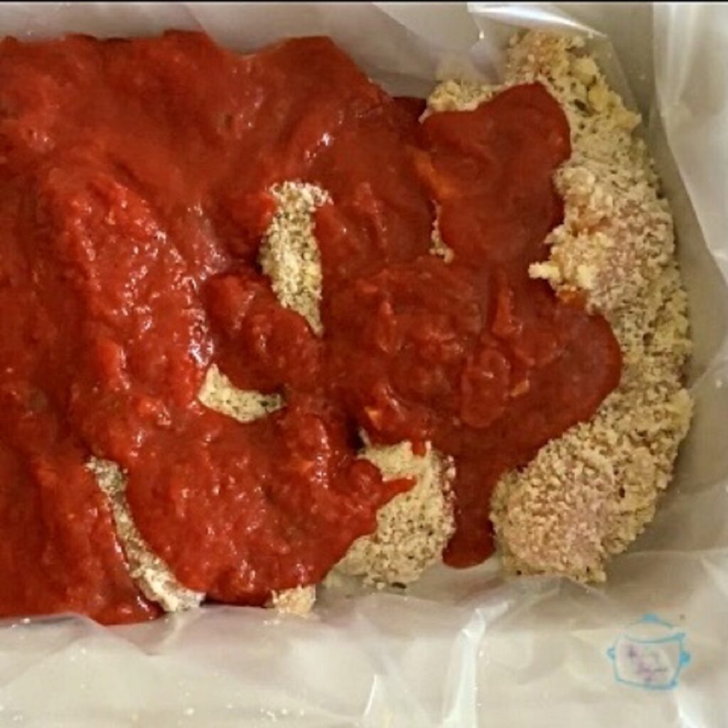 raw breaded chicken in a slow cooker partially covered with sauce