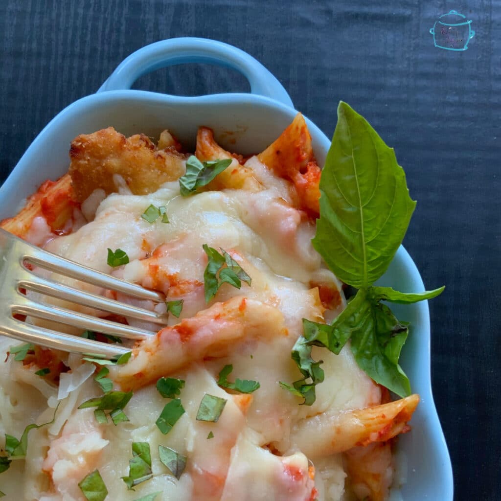 close up of a blue bowl with noodles, cheese sauce and a sprig of fresh basil. a fork is about to dig in