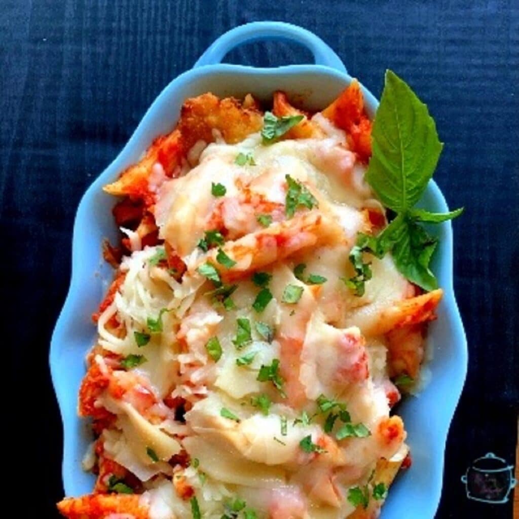 close up of a blue bowl with noodles, cheese sauce and a sprig of fresh basil